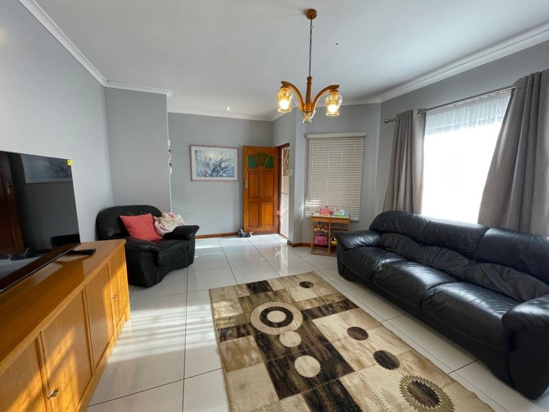 A bright living room featuring tiled flooring, cove cornicing, and a timber entrance door, offering a functional and well-lit space.