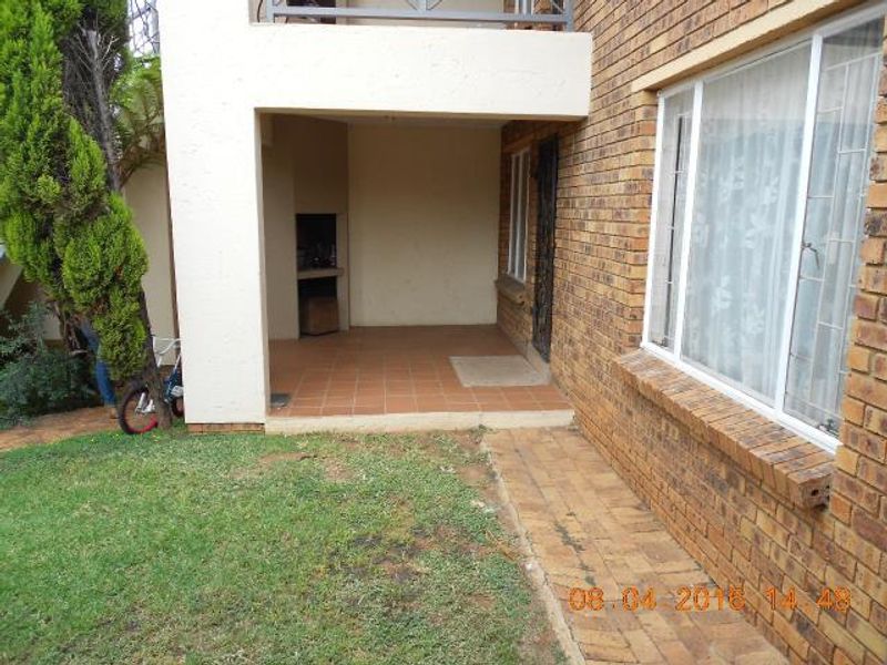Covered patio area featuring a built-in braai, tiled flooring, and direct access to the garden and paved walkway.