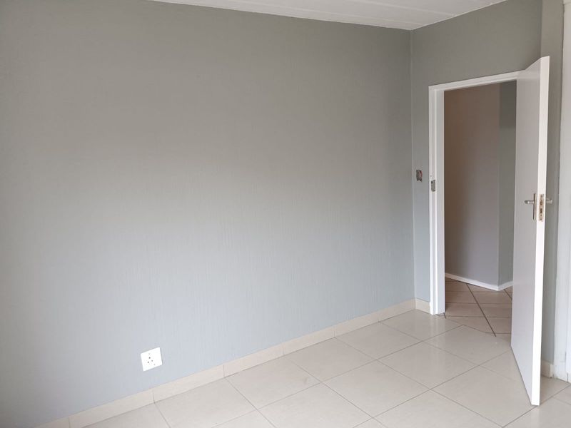 A clean, empty bedroom featuring neutral grey walls, tiled flooring, and a white internal door leading to an adjacent space.