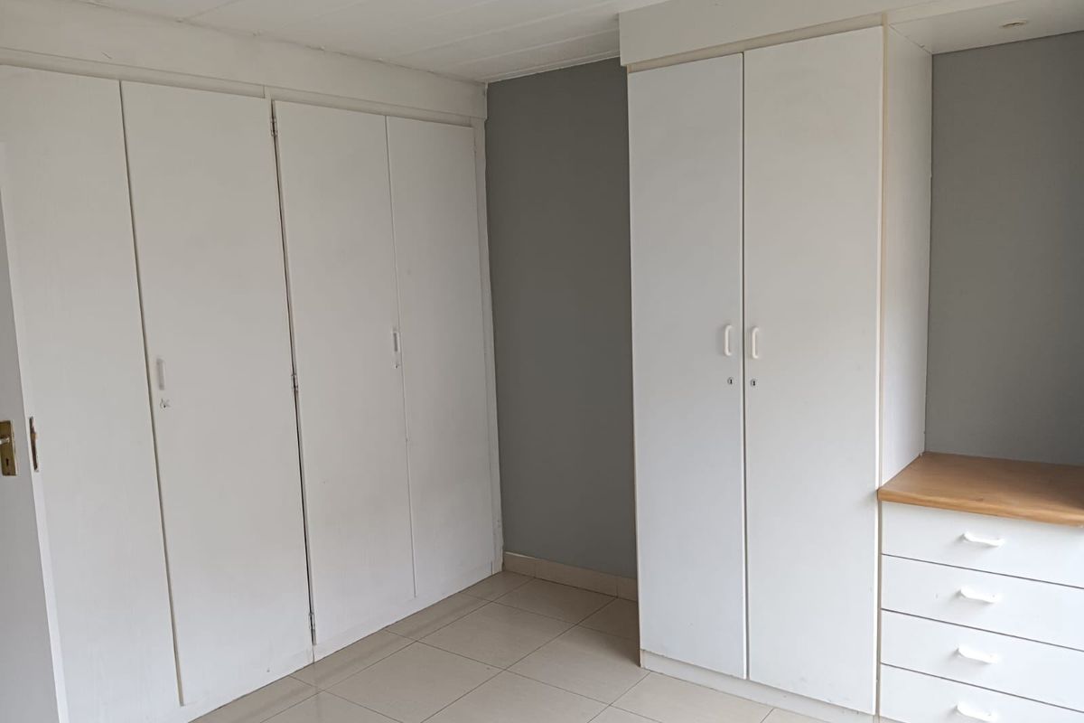A bedroom featuring extensive built-in cupboard storage and a built-in vanity unit with drawers, finished with neutral tiled flooring.