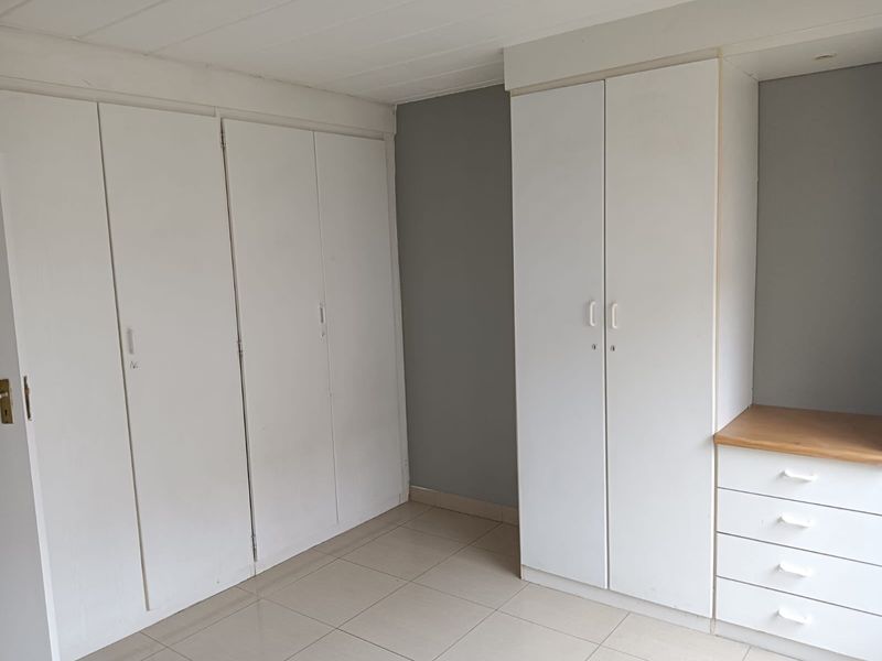 A bedroom featuring extensive built-in cupboard storage and a built-in vanity unit with drawers, finished with neutral tiled flooring.