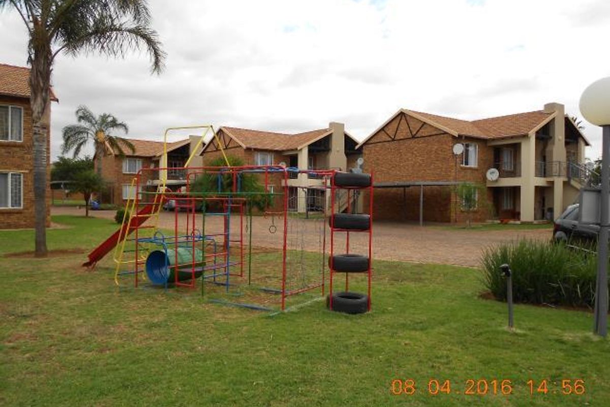 Exterior view of a townhouse complex featuring brick facades, tiled roofs, a paved driveway, and a communal garden area with playground equipment.