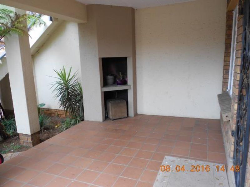 A covered patio area featuring tiled flooring and a built-in braai, providing a functional outdoor space for entertainment.