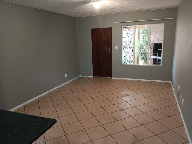 An empty, open-plan living area featuring neutral grey walls, tiled flooring, and a secure timber entrance door with window security bars.