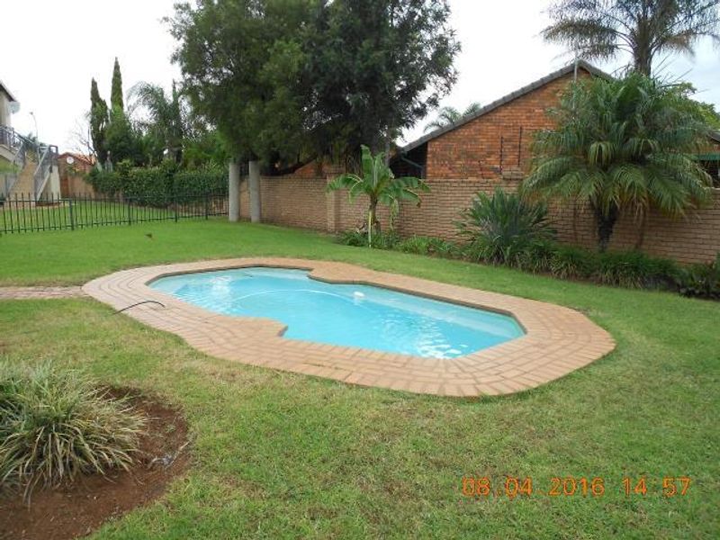 A private backyard featuring a swimming pool with brick coping, surrounded by a well-maintained lawn and a brick boundary wall.