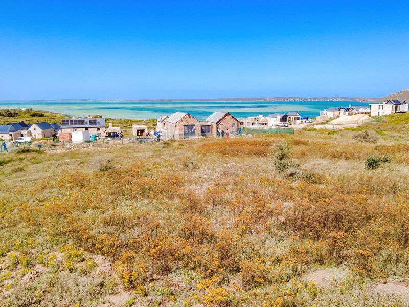 An aerial view of a vacant residential plot overlooking a coastal landscape and nearby residential development.