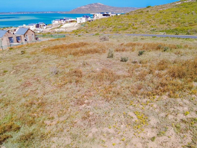 An aerial view of a vacant residential plot featuring natural coastal vegetation and scenic water views in the surrounding area.