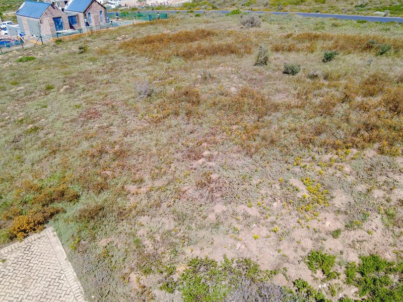 Aerial view of a vacant residential plot featuring natural vegetation and an adjacent paved driveway area.