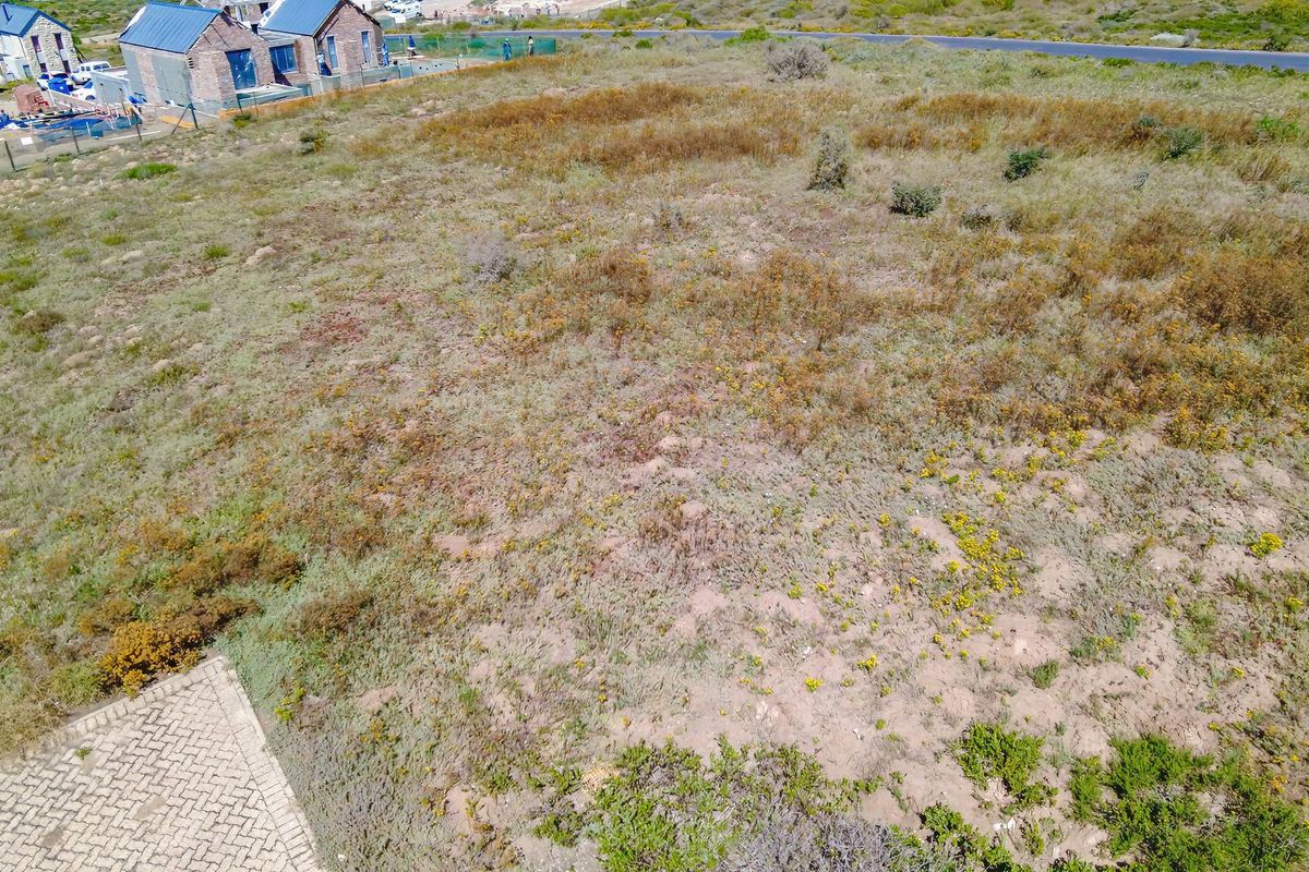 Aerial view of a vacant residential plot featuring natural vegetation and an adjacent paved driveway area.