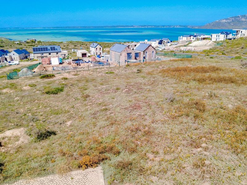An aerial view of a vacant residential plot overlooking a coastal landscape and nearby housing development.