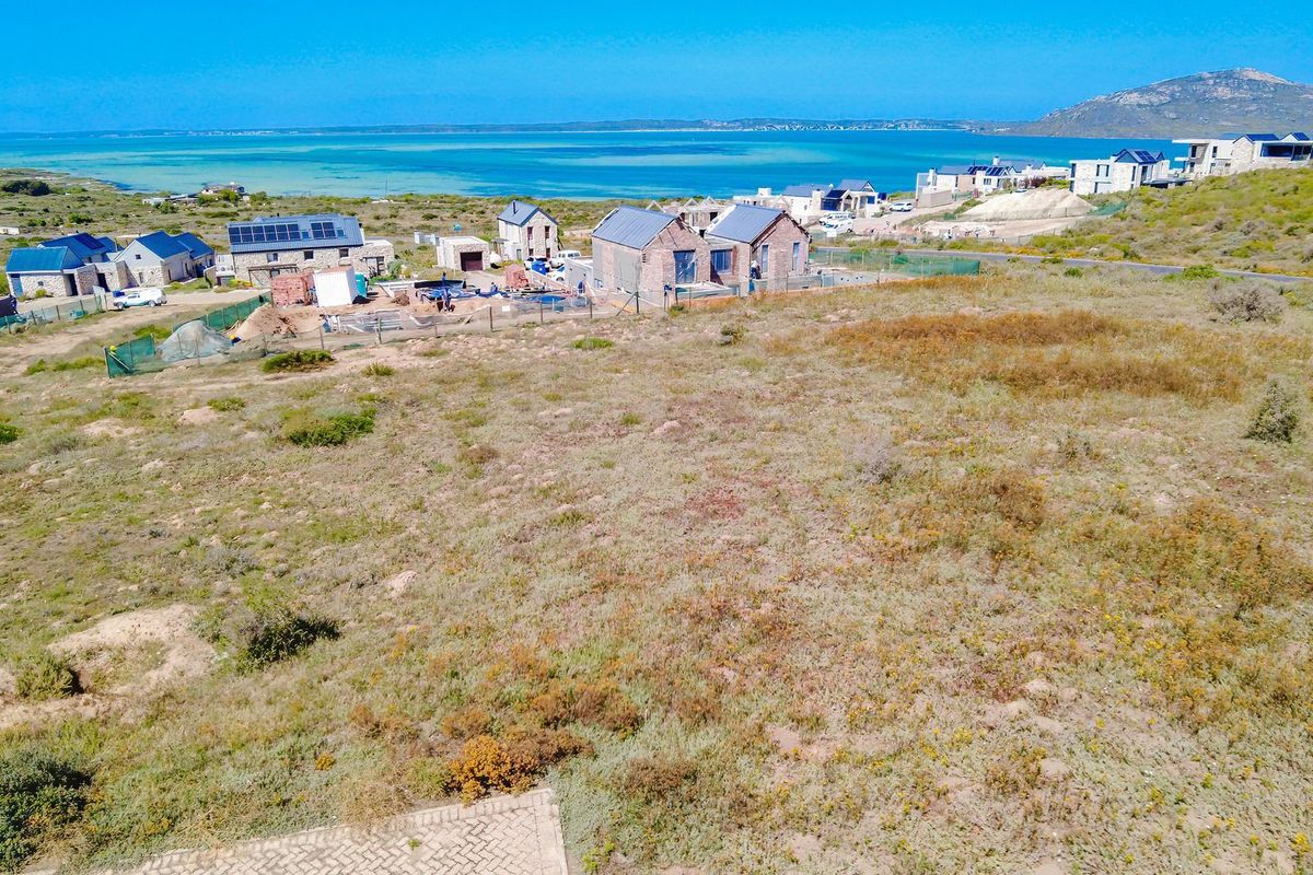 An aerial view of a vacant residential plot overlooking a coastal landscape and nearby housing development.