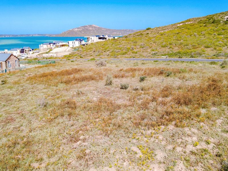 An aerial view of a vacant residential plot featuring natural coastal vegetation with scenic ocean and mountain views in the background.