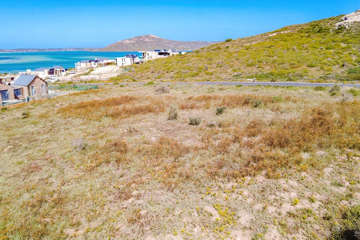 An aerial view of a vacant residential plot featuring natural coastal vegetation with scenic ocean and mountain views in the background.
