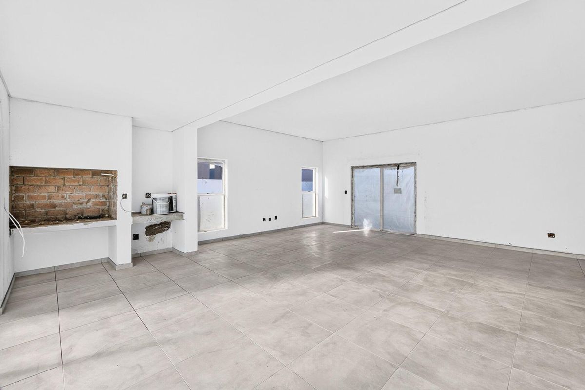 Spacious, empty living area featuring large format floor tiles, sliding door access, and an unfinished built-in fireplace ready for renovation.