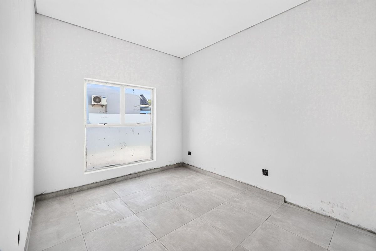 An empty bedroom featuring neutral tiled flooring and a sliding window, currently awaiting final finishes and skirting installation.