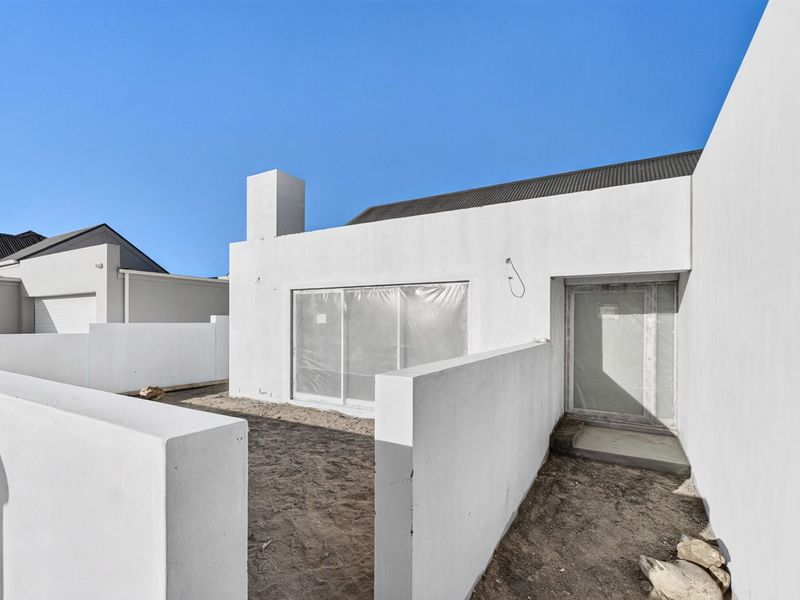 Rear exterior view of a modern home featuring white rendered walls, a chimney, and a sliding glass door, currently undergoing final landscaping.