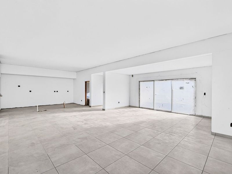 A spacious, unfinished open-plan living area featuring large format floor tiles, sliding glass doors, and exposed utility connections, ready for final interior finishes.