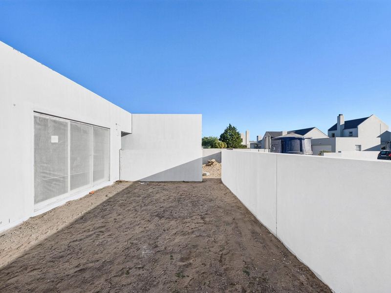 A rear exterior view of a modern home featuring a large sliding glass door and an unlandscaped backyard area enclosed by boundary walls.