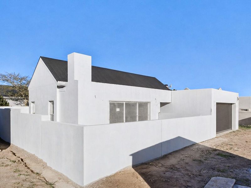 Rear view of a modern white house featuring a corrugated metal roof, chimney, and attached garage with a secure boundary wall.