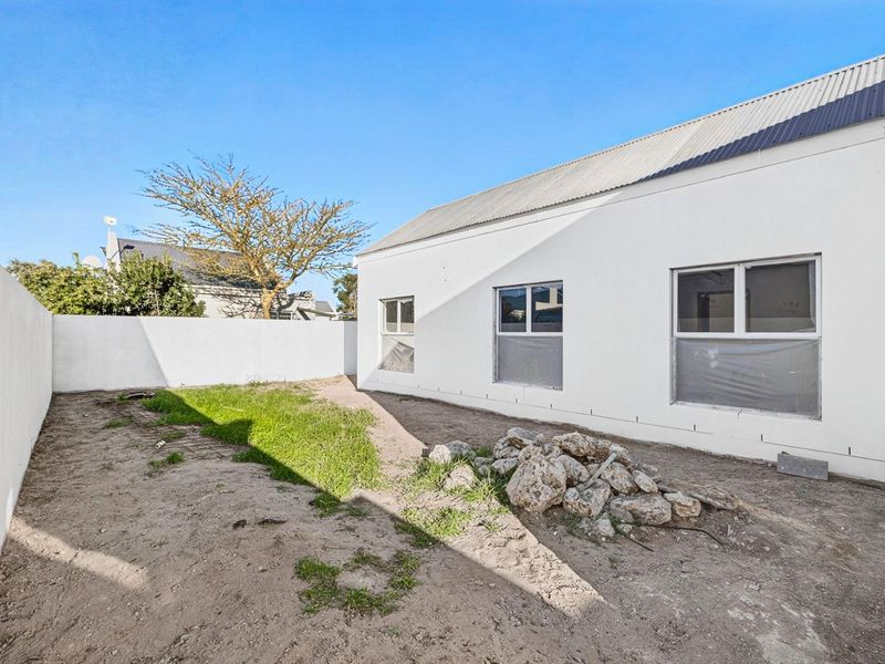 Rear exterior view of the property featuring a white facade, corrugated metal roof, and an unfinished garden area requiring landscaping.