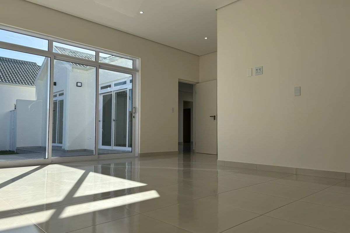 A bright, empty living area featuring polished tile flooring, recessed lighting, and large sliding glass doors that provide access to the exterior.