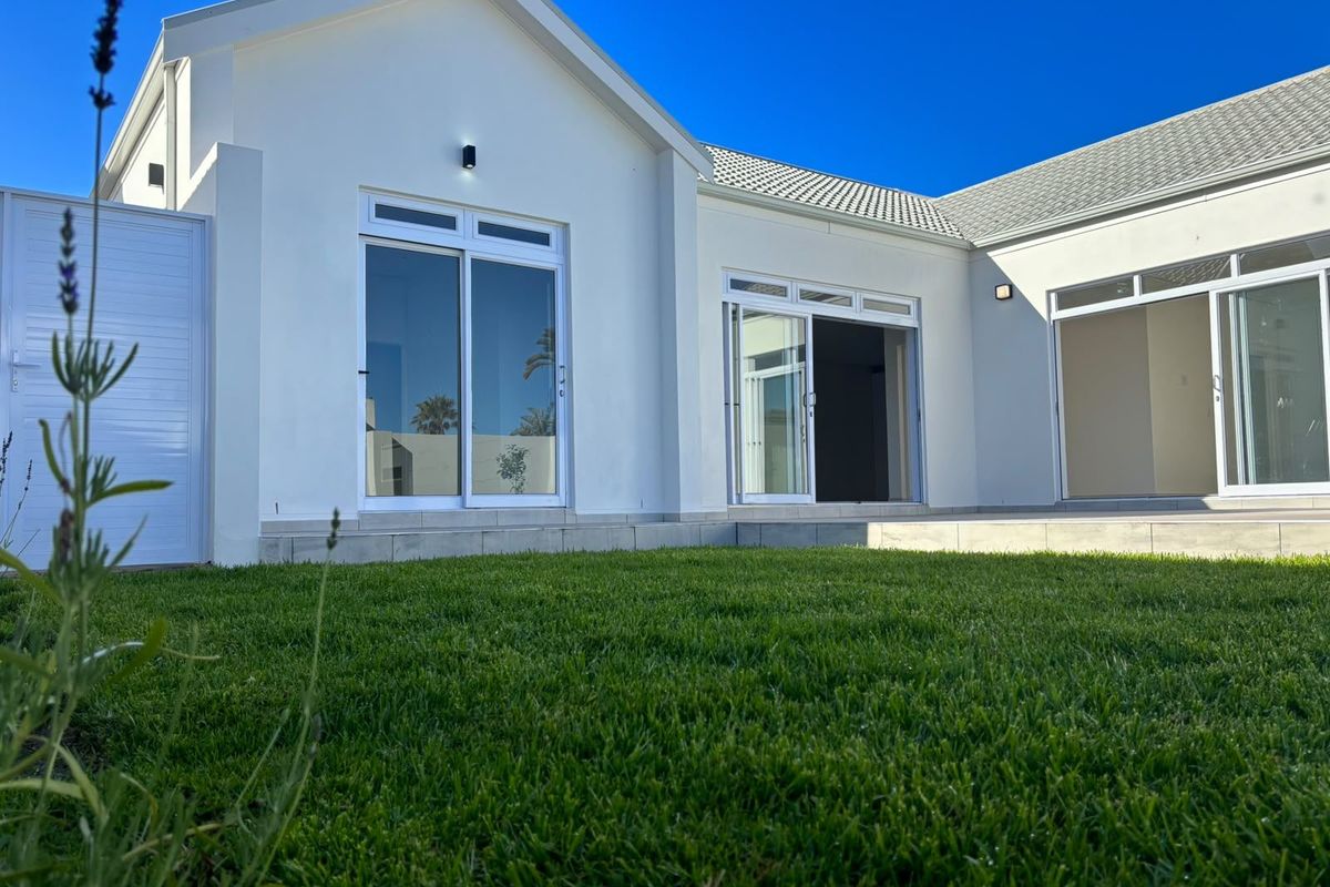 A well-maintained rear exterior view of the house featuring a manicured lawn, tiled patio area, and multiple sliding glass doors providing indoor-outdoor flow.