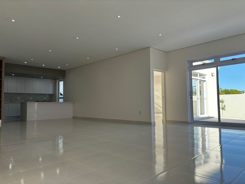 Spacious open-plan living area featuring polished porcelain tiles, recessed lighting, and a modern kitchen with built-in cabinetry, flowing seamlessly to an outdoor patio.