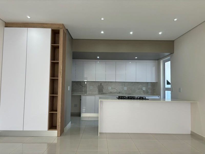 Modern kitchen featuring sleek white cabinetry, stone countertops, a built-in gas hob, and high-quality tiled flooring in a clean, minimalist design.