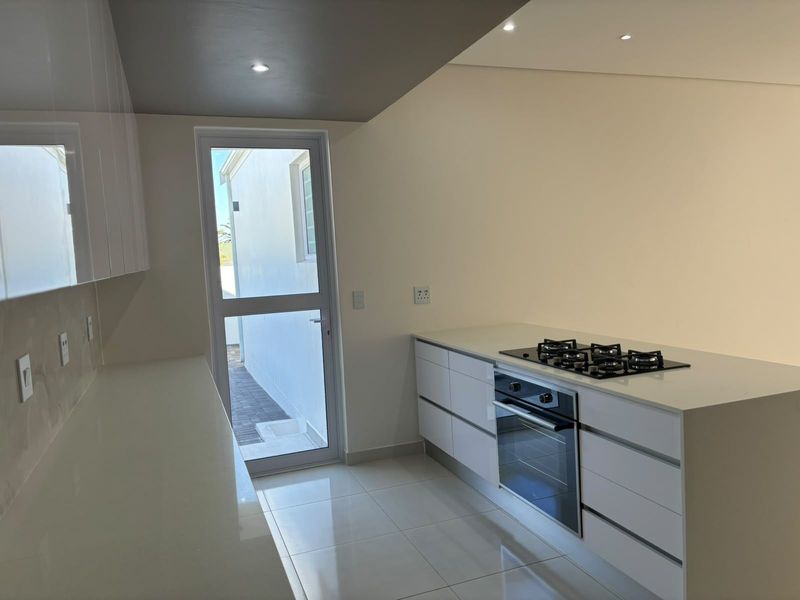 Modern kitchen featuring white gloss cabinetry, stone countertops, built-in oven, gas hob, and tiled flooring with direct access to the exterior.