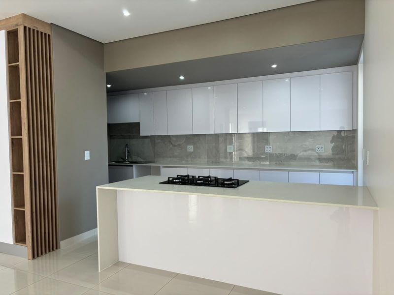 Modern kitchen featuring sleek white cabinetry, stone countertops, a central island with a gas hob, and elegant timber slat detailing.