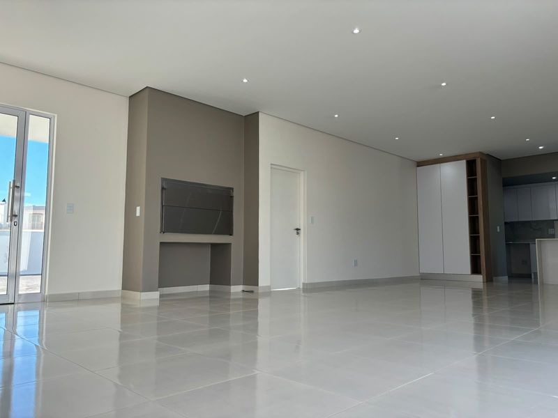 Spacious open-plan living area featuring polished porcelain tiles, recessed lighting, a built-in braai, and seamless access to the outdoor patio.