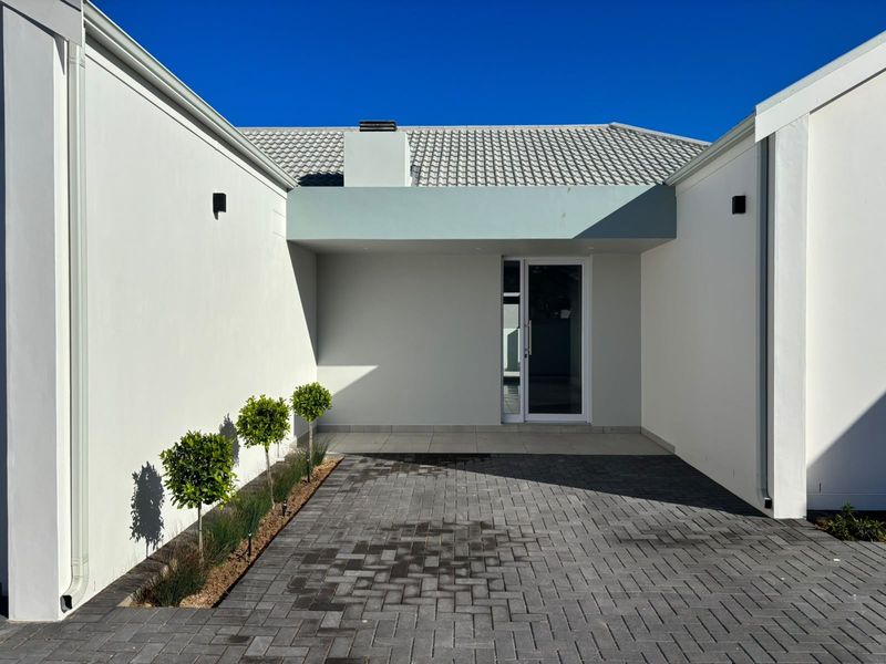 A modern front entrance featuring a paved driveway, clean white rendered walls, and a contemporary glass-panelled front door under a covered entryway.
