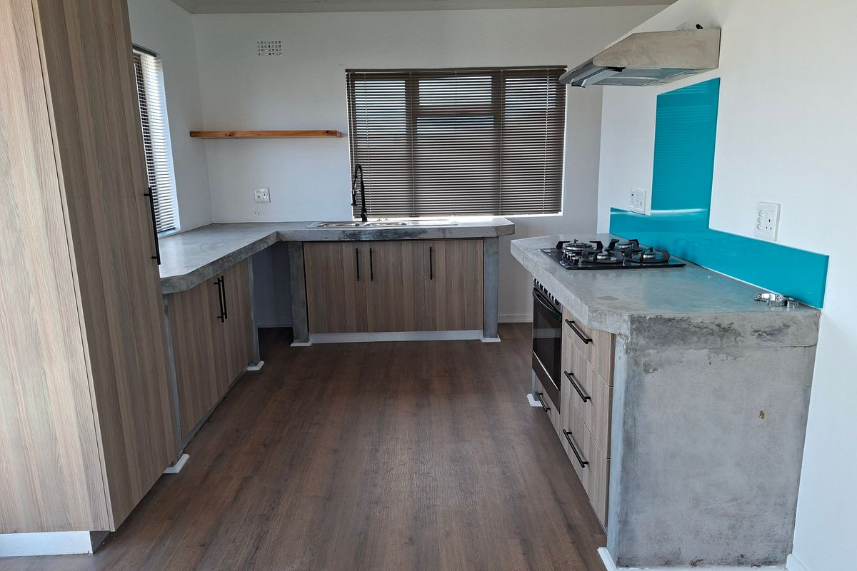 Modern kitchen featuring concrete countertops, wood-look cabinetry, gas hob, extractor fan, and integrated oven with a vibrant blue glass splashback.