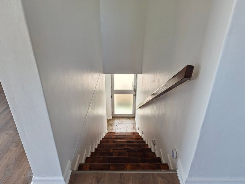 A view looking down a wooden staircase towards a glass panel door leading to an exterior landing.