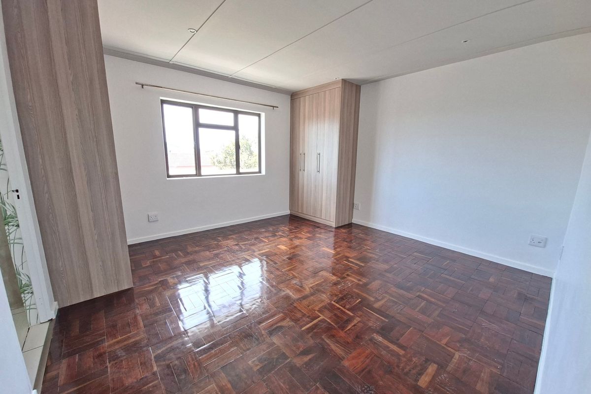 A bright, empty bedroom featuring polished parquet flooring and built-in wooden cupboards, offering a clean and neutral space ready for personalization.