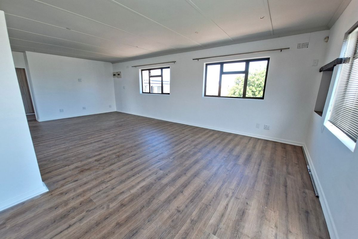 A spacious, empty living area featuring modern laminate flooring, neutral white walls, and large windows that provide ample natural light.