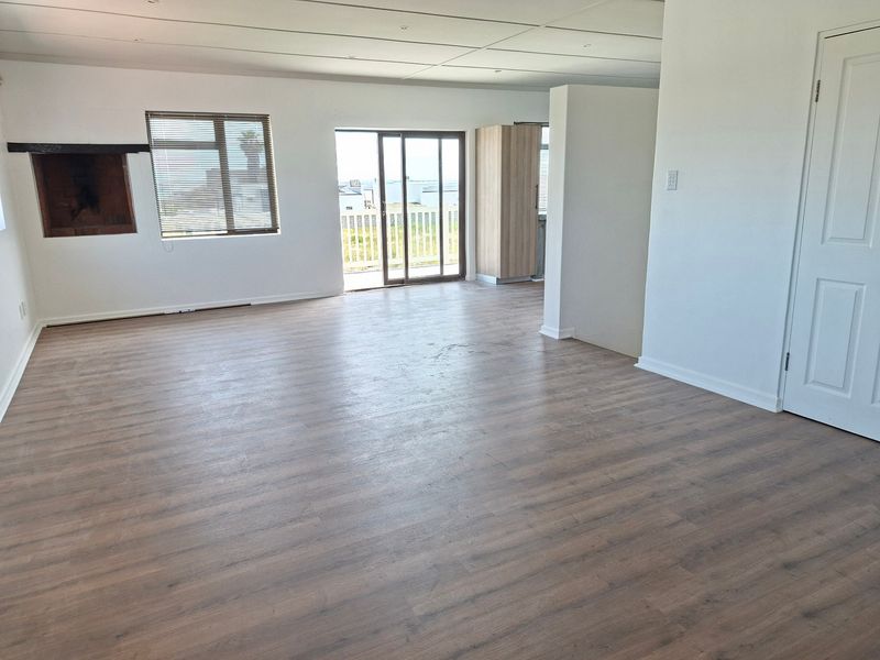 Spacious open-plan living area featuring laminate flooring, a built-in fireplace, and sliding glass doors leading to an outdoor space.