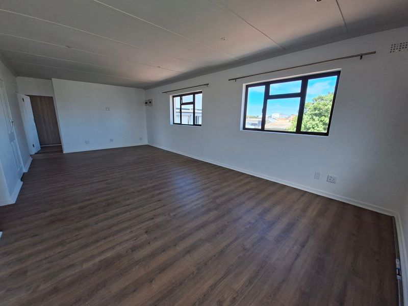 A spacious, empty living area featuring modern laminate flooring, neutral walls, and large aluminium-framed windows that provide ample natural light.