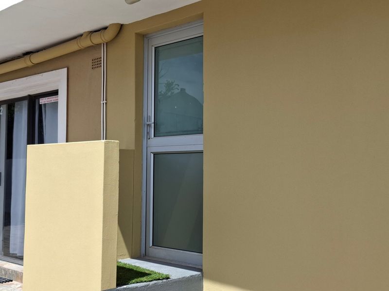 A view of the exterior rear wall featuring an aluminium door, concrete step, and external plumbing fixtures.