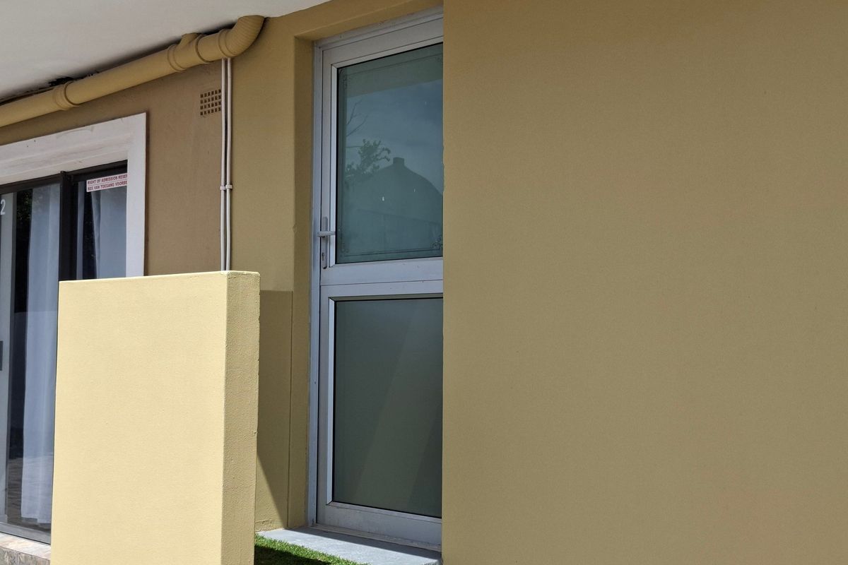A view of the exterior rear wall featuring an aluminium door, concrete step, and external plumbing fixtures.