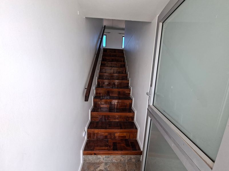 An entry area featuring a wooden staircase with a handrail, leading to an upper level, with tiled flooring and a glass door entrance.