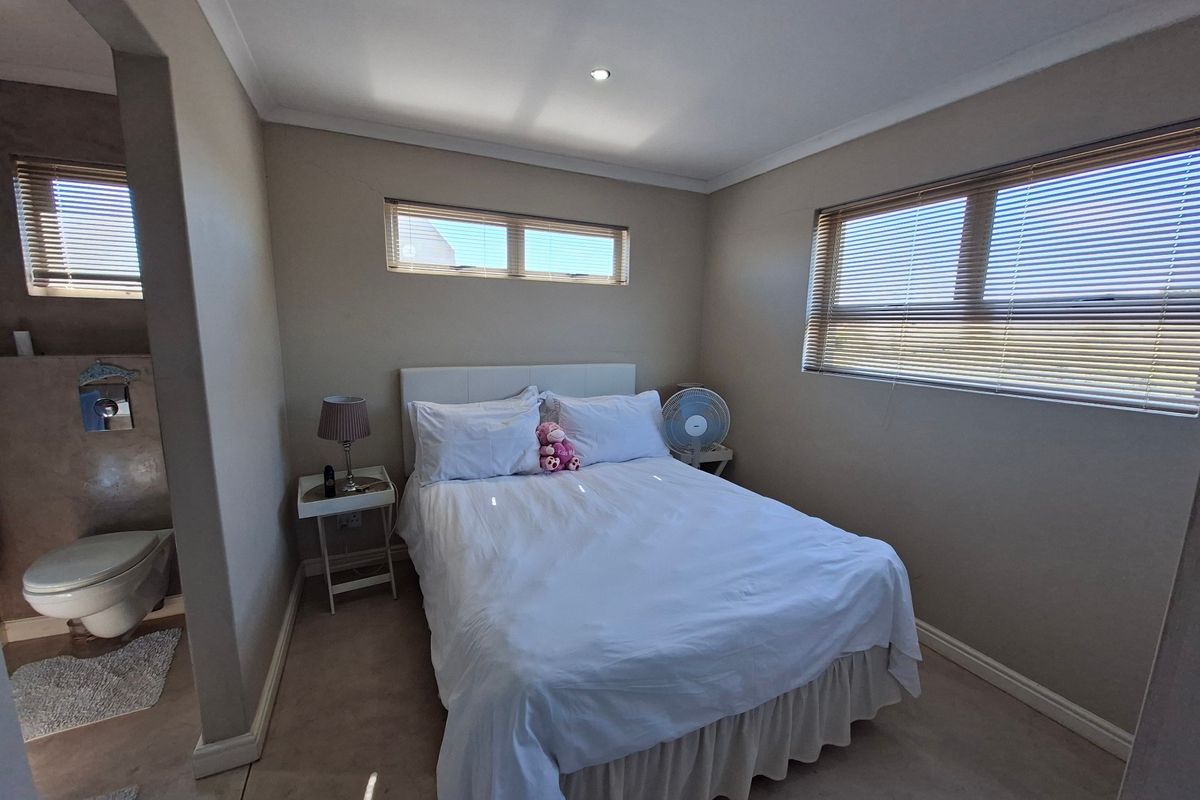 A well-lit bedroom featuring neutral walls, venetian blinds, and an integrated en-suite bathroom with a toilet.