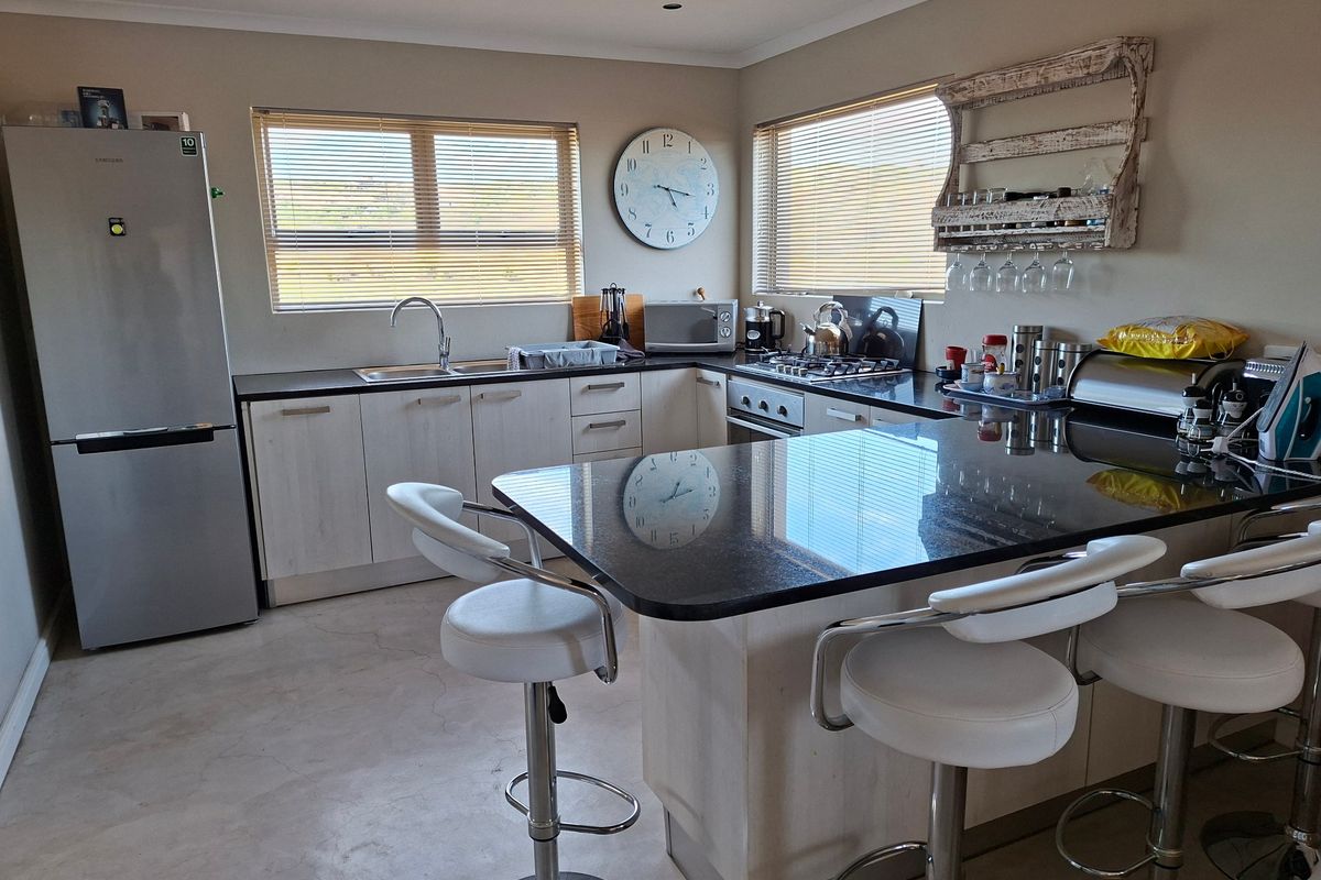 A functional kitchen featuring granite countertops, light-toned cabinetry, a gas hob, and an integrated breakfast bar with ample natural light.