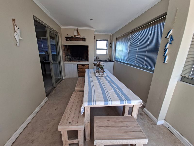 Enclosed patio area featuring a built-in braai, concrete flooring, and large windows with venetian blinds, suitable for indoor-outdoor entertaining.