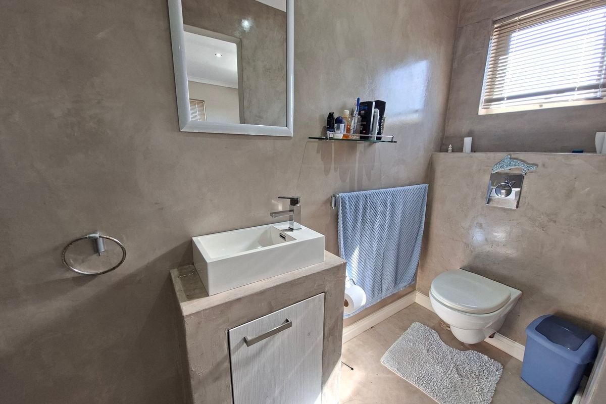 Modern bathroom featuring a wall-mounted toilet, vessel sink with vanity cabinet, and polished concrete-style wall finishes.