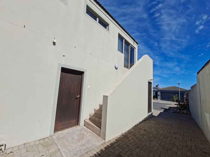Rear exterior view of the apartment building featuring a paved driveway, external staircase, and access doors.