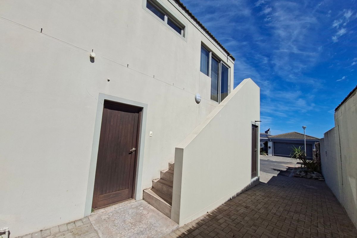 Rear exterior view of the apartment building featuring a paved driveway, external staircase, and access doors.