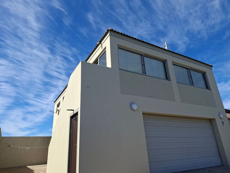 Exterior view of a modern apartment building featuring a garage, side entrance, and upper-level windows under a clear blue sky.