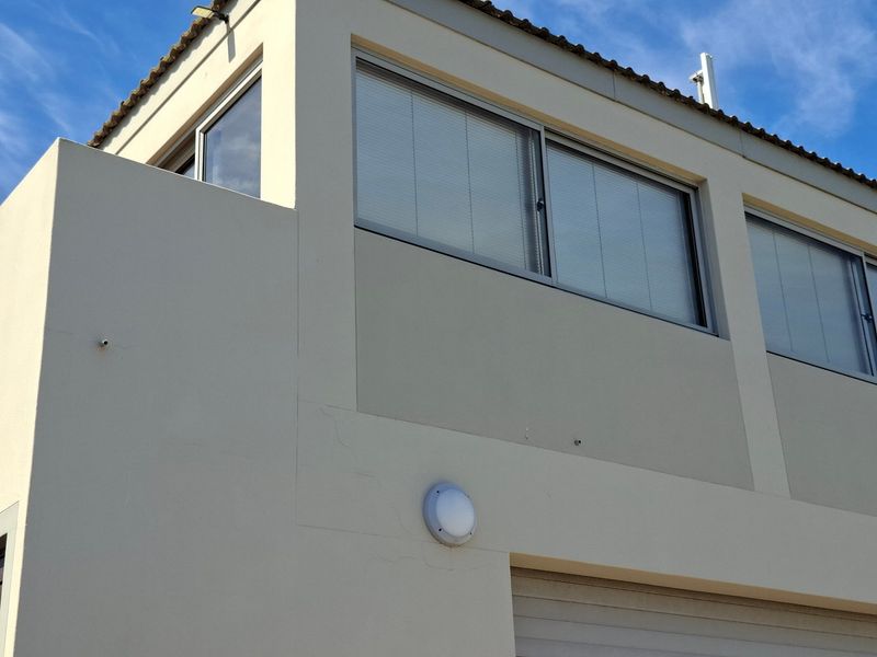 A view of the upper level exterior facade featuring plastered walls, sliding windows, and a tiled roof section.