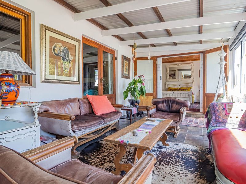 A bright, enclosed patio area featuring exposed beam ceilings, tiled flooring, and large timber-framed glass doors providing access to the interior living spaces.